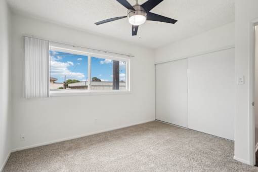 A room with a ceiling fan and a window overlooking a residential area.