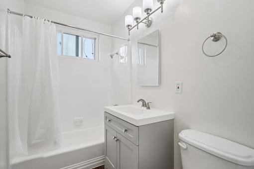 A white bathroom with a sink, mirror, and tub.
