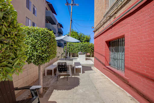 A patio with a table and chairs is surrounded by a brick wall and a green bush.