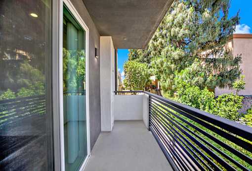 A balcony with a black railing and a glass door leading to a lush green outdoor area.