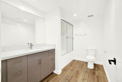 A white toilet sits in a bathroom with a white sink and wooden floors.
