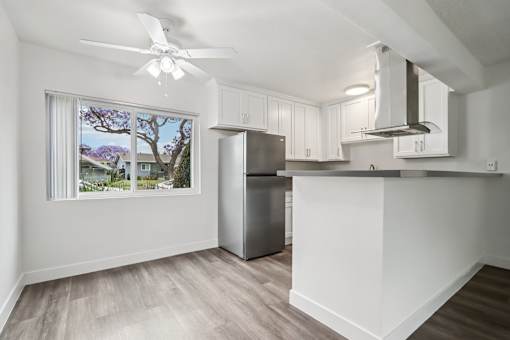 A kitchen with a refrigerator, a ceiling fan, and a window overlooking a residential area.