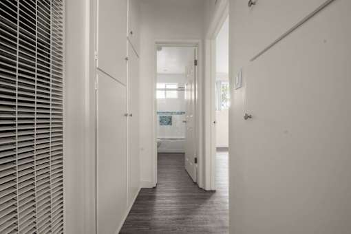 a long hallway with white walls and white doors and a white bathroom with a window