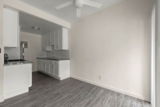 a white kitchen and living room with a ceiling fan