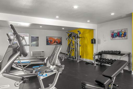 A gym with a rowing machine, a bench press, and a yellow wall at Sunset Square, West Covina, 91790