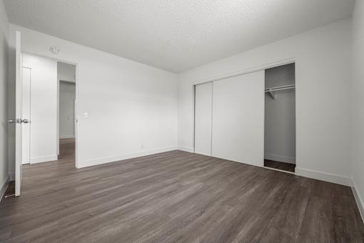 A room with white walls and wood flooring with a door on the left and a closet on the right at Sunset Square, West Covina, 91790