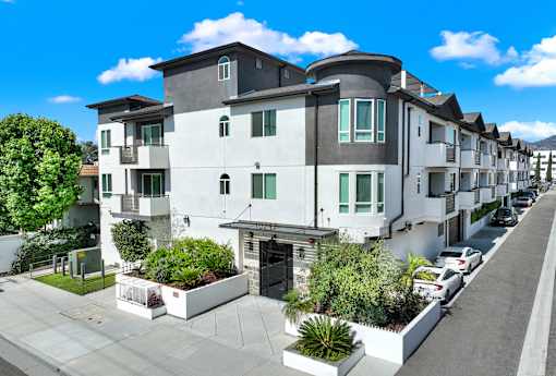 A row of modern townhouses with white and grey exteriors and green plants in front.