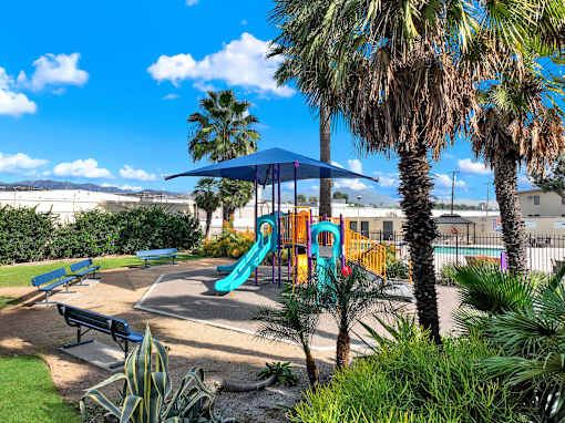 A playground with a blue slide and a blue umbrella.