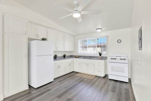 A white kitchen with a refrigerator, oven, and a ceiling fan.