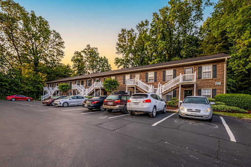 A parking lot with several cars parked in front of a building with a red car parked in the far left.