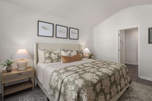 A bedroom with a large bed and a nightstand with a lamp and plant.