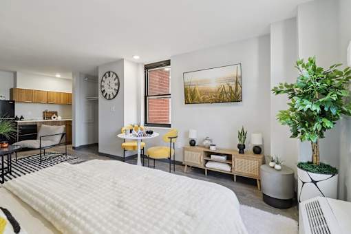 A modern bedroom with a large bed and a kitchen area in the background.
