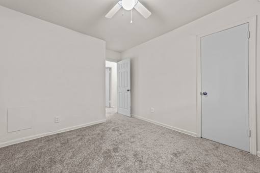 A room with a carpeted floor and a ceiling fan.