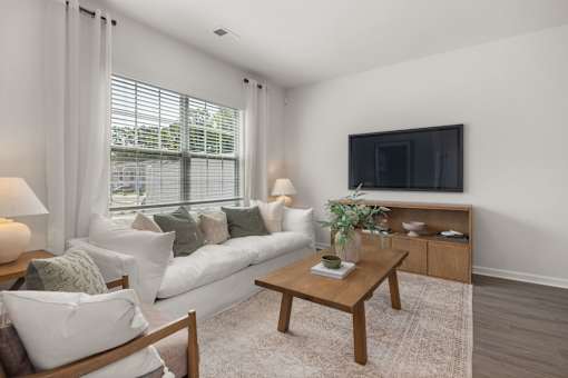 A living room with a white couch, a wooden coffee table, and a flat screen TV mounted on the wall.