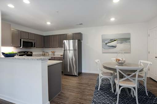 A kitchen with a refrigerator, microwave, and a dining table with chairs.