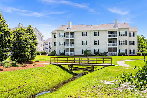 A white apartment building with a yellow bridge over a small stream.