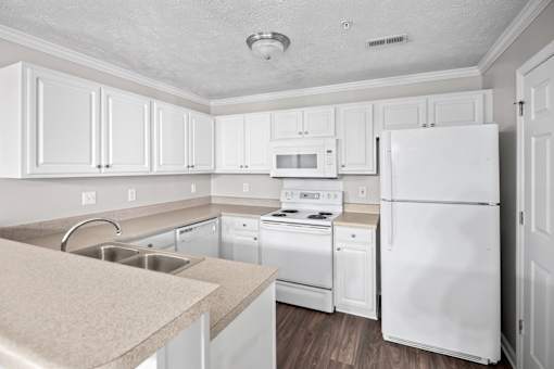 A white kitchen with a refrigerator, sink, and stove.