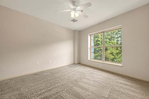 A room with a ceiling fan and a window showing trees outside.