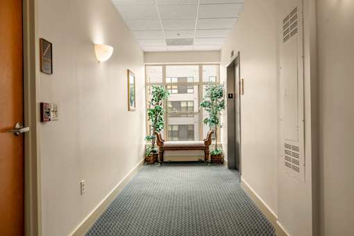 A long hallway with a door on the left and a window with a view of a building on the right.