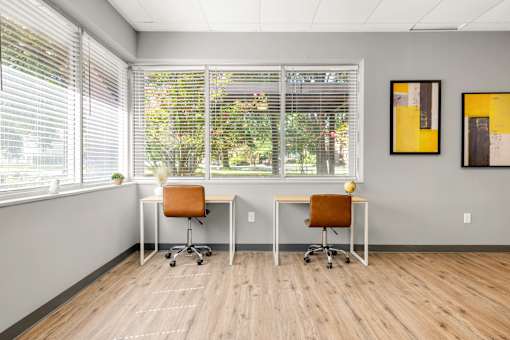 Two desks with chairs in front of a window with blinds.