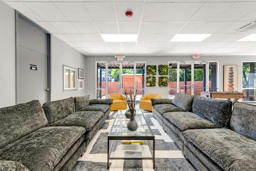 A grey couch is in the middle of a room with a glass table in front of it.