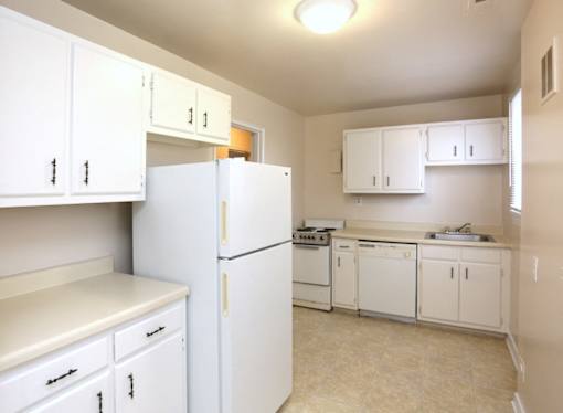 View of kitchen model with white cabinets, refrigerator, dishwasher, range