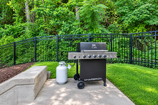 A Charbroil gas grill is set up on a concrete slab in a backyard.