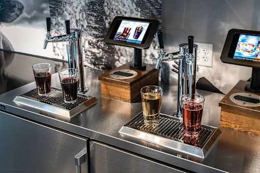 A stainless steel beer tap with a glass of beer on the right side.