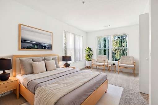 A bedroom with a large bed, two chairs, and a painting on the wall.