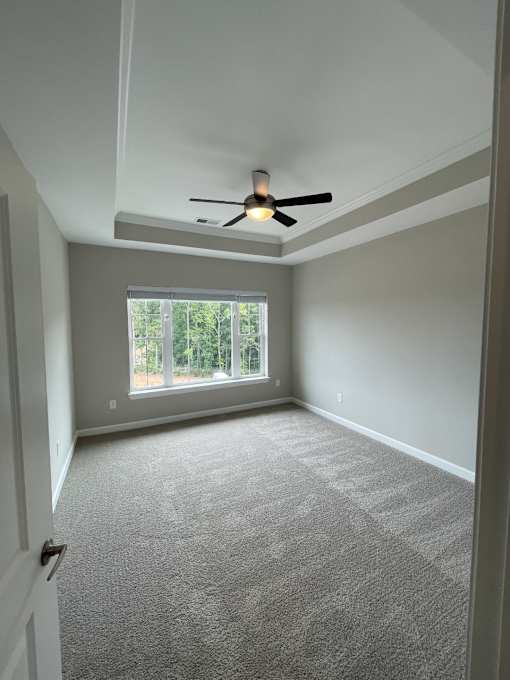 A bedroom in an apartment with a ceiling fan and a window looking out to Clayton, NC.