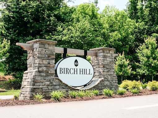 A sign that says Birch Hill stands in front of a green forest.