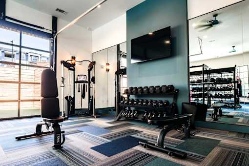 A gym with a variety of equipment including a bench, weights, and a television.