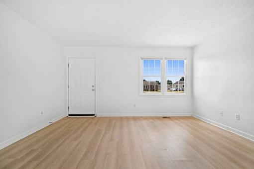 A room with a white door and a window with a view of houses across the street.