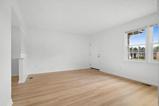 A room with wooden flooring and a window showing a view of a house.