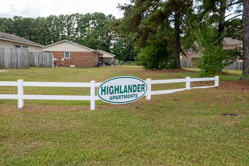 A sign that says Highlander Apartments stands in a grassy field.