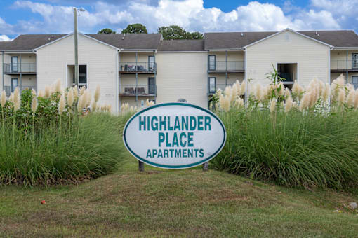 A sign for Highlander Place Apartments in front of a building.