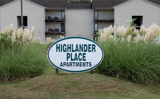 A sign for Highlander Place Apartments in front of a building.