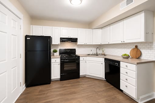 A black refrigerator is in a kitchen with white cabinets.