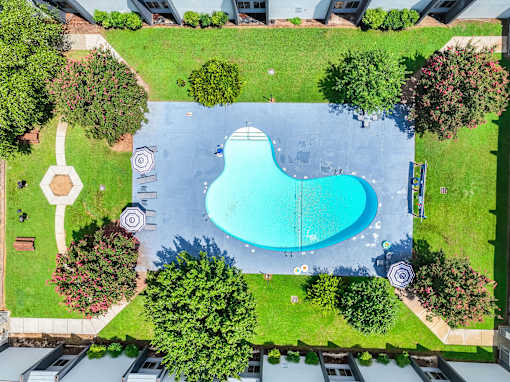 An aerial view of a swimming pool surrounded by trees and a grassy area.