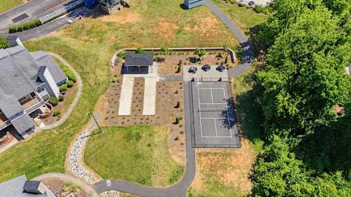 A tennis court is surrounded by a grassy area and a few trees.