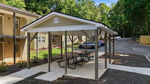 A covered picnic area with a table and chairs is located in front of a building.