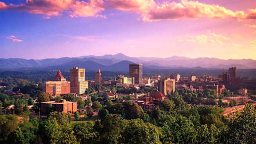A cityscape with buildings and trees under a pink and blue sky.