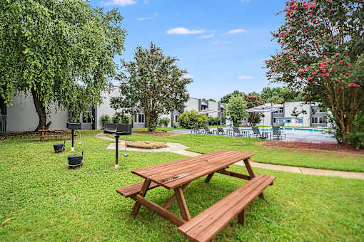A picnic table and bench are in the foreground of a grassy area.