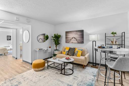 A living room with a yellow ottoman, a white couch, a coffee table, and a dining table with chairs.