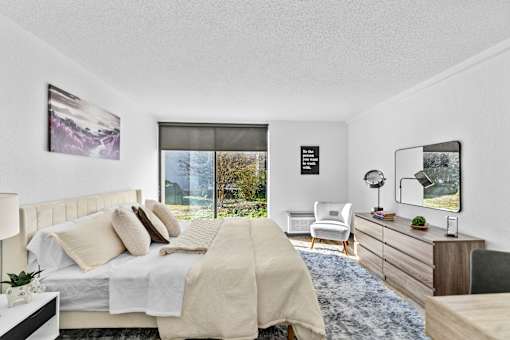 A bedroom with a large bed, a chair, and a window overlooking a garden.