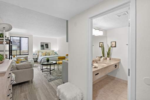 A white room with a bed, a couch, a table, and a plant.