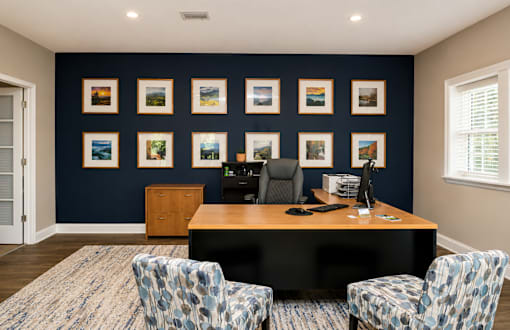 A room with a desk, chairs and pictures on the wall.