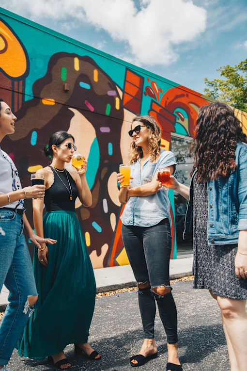 Four women are standing in front of a colorful mural.