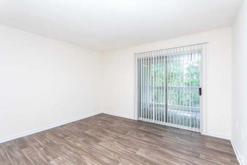 A room with a sliding glass door and wooden flooring.