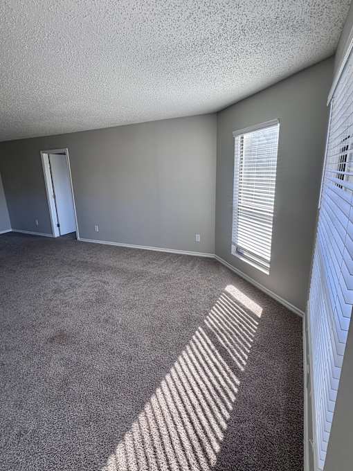 A room with a carpeted floor and a window with blinds.